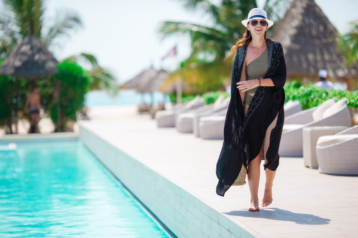 Beautiful young woman relaxing on the edge of outdoor pool in luxury rich hotel