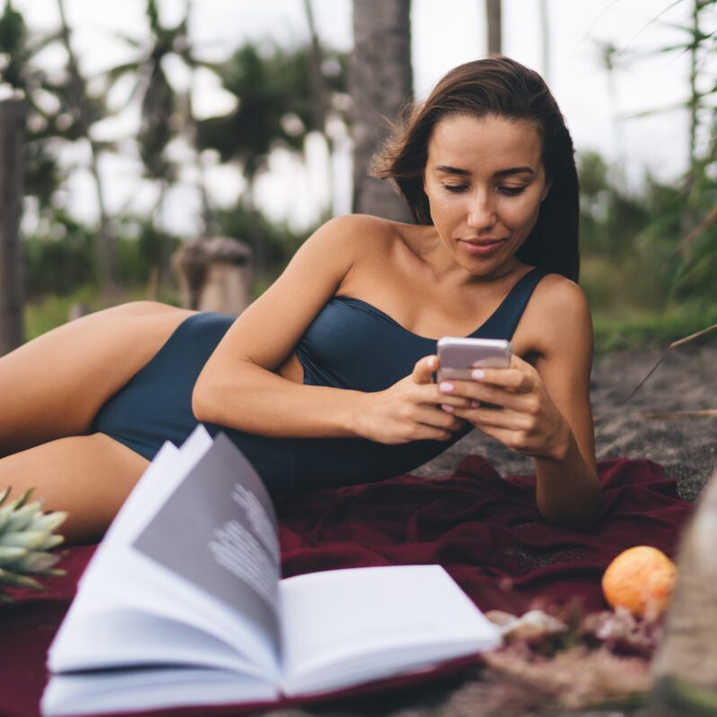 Young female travel blogger in swimwear booking hotel on website during summer vacations for recreat